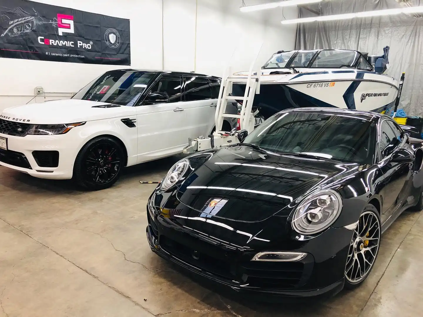 White Range Rover Sport and black Porsche 911 Turbo inside the shop, a boat on its trailer behind them